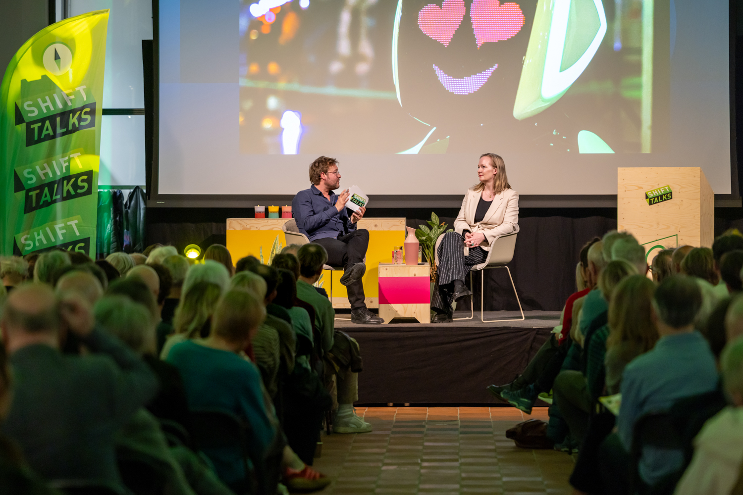Twee personen op een podium met publiek op de voorgrond